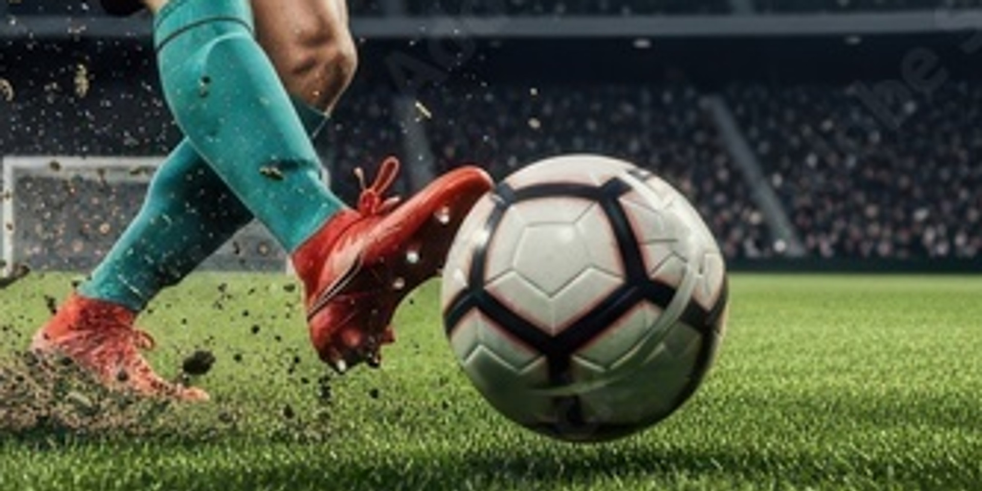 Beine in grüner Sportbekleidung und roten Fußballschuhen schießen einen Fußball auf dem Stadionrasen